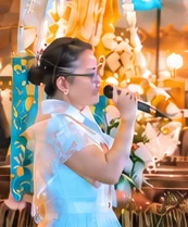 Florane in a white-and-blue dress singing into a microphone at a church celebration